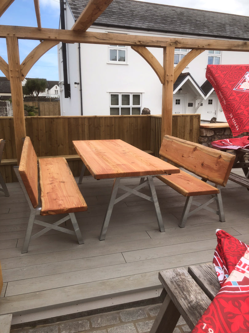 Handcrafted outdoor garden furniture on a balcony featuring galvanised steel legs and a live edge table and benches.