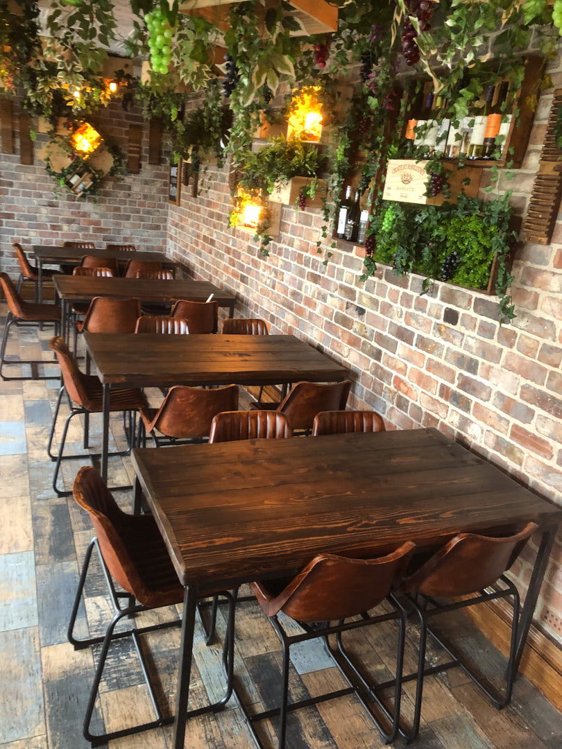 Dining area with custom built wooden tables and chairs against a brick wall with decorative plants.