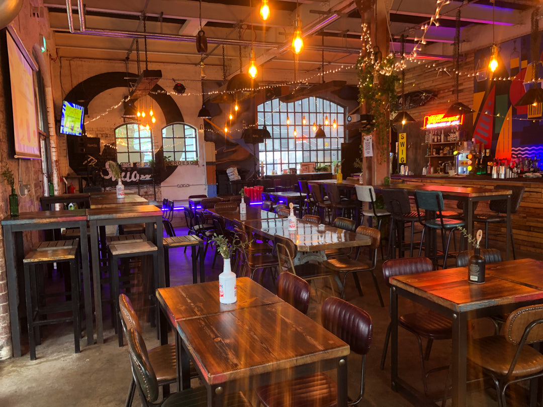 Interior of The Swigg with custom built wooden tables and chairs, hanging lights, and large windows.