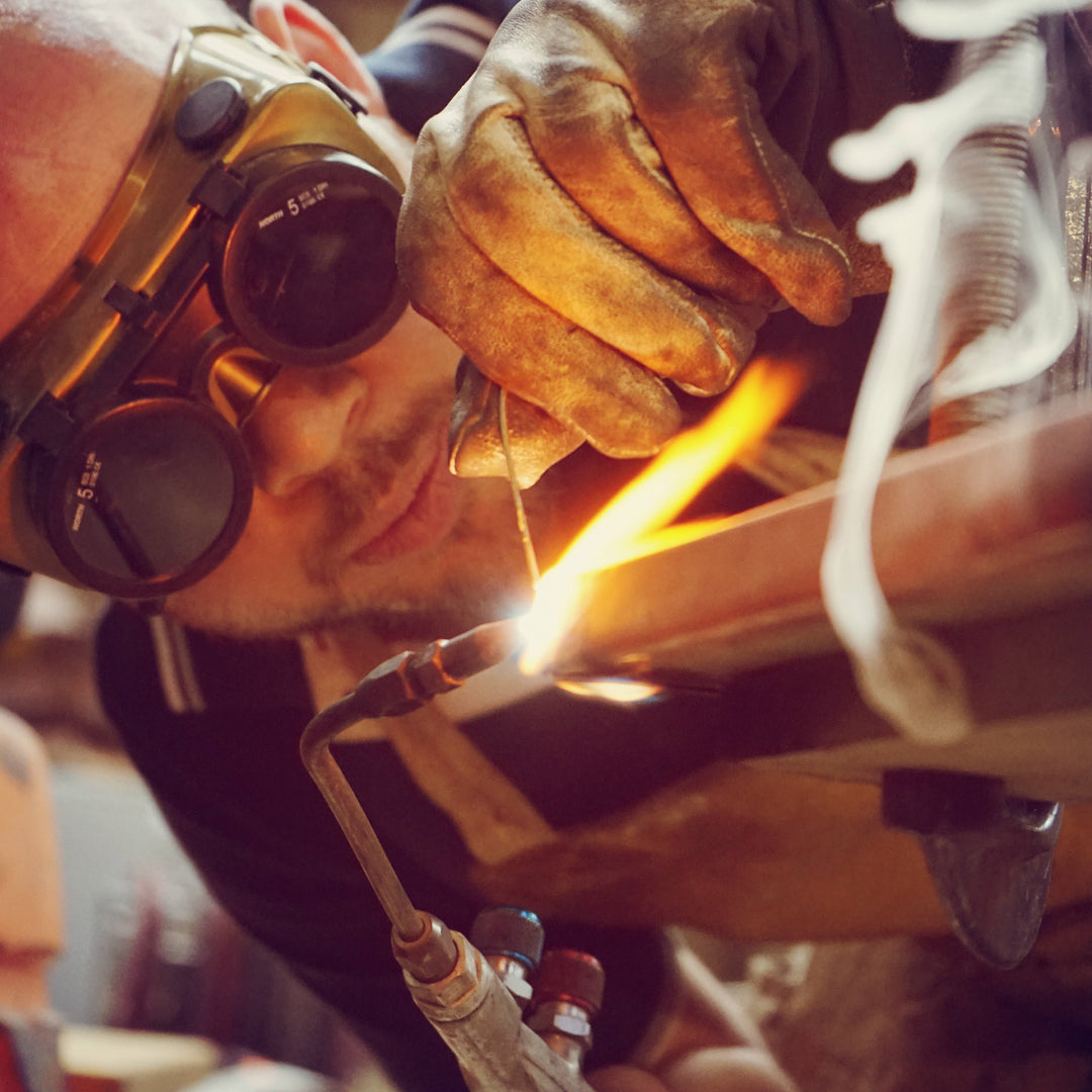 Person welding with protective gear in a workshop setting.