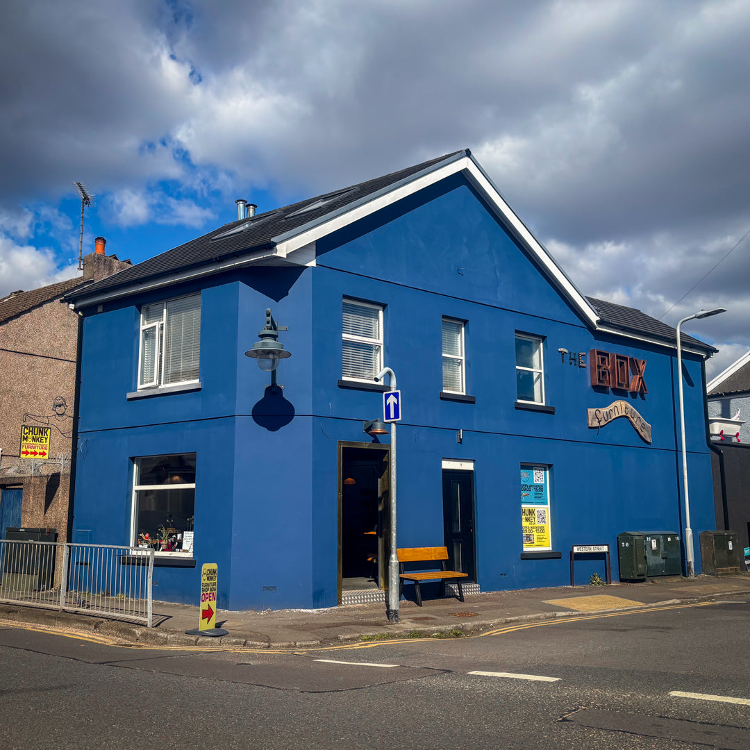 Blue building with 'The BOX Furniture' sign and 'Chunk Monkey' sign on a street corner under a cloudy sky.